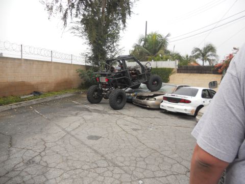 1986 Ford Bronco - A custom off-road buggy is parked on top of two damaged sedans in a lot.