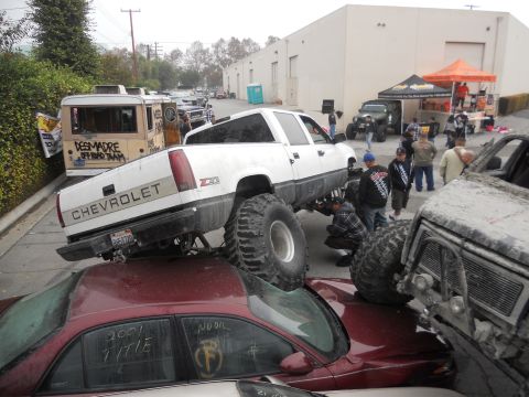 1986 Ford Bronco - A modified Chevrolet pickup truck is shown crushing a sedan, with onlookers observing the scene.