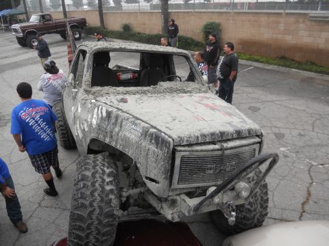 1986 Ford Bronco - Mud-covered pickup truck with large tires, parked outdoors with people around. Another truck is in the background.