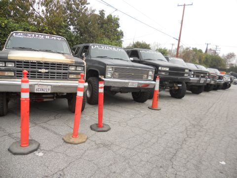 1986 Ford Bronco - Several lifted Chevrolet K5 Blazers and pickup trucks are parked in a row, some displaying custom decals.