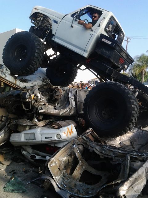 1986 Ford Bronco - A monster truck is positioned atop a pile of mangled vehicles, with a driver inside the cab.
