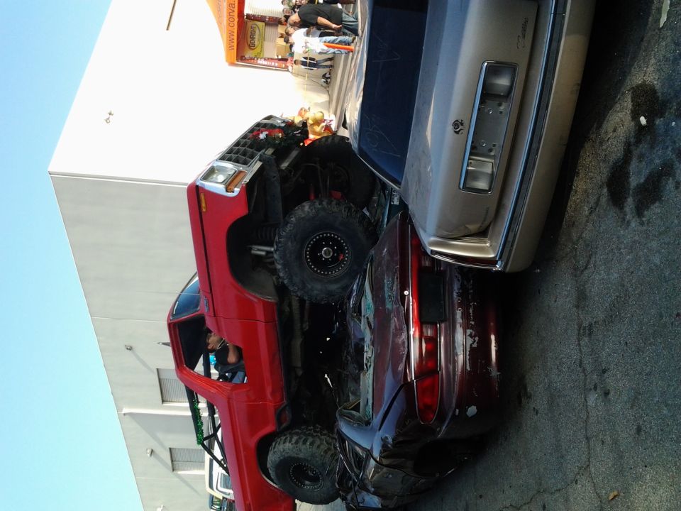 Red 1986 Ford Bronco crushing a red car, lifted with large tires