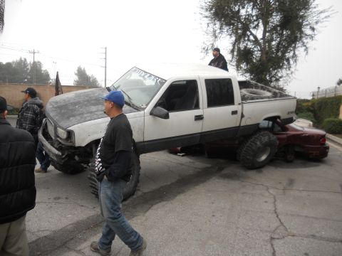 1986 Ford Bronco - A heavily modified pickup truck is positioned on top of a smaller car, with onlookers present.