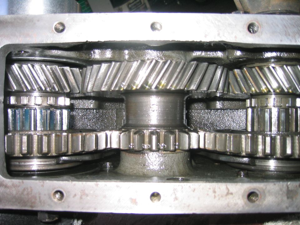 Close-up of metal transmission gears inside a housing, showing helical cut teeth and lubrication