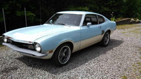 1973 Ford Maverick - A two-tone 1973 Ford Maverick coupe is viewed from the front three-quarter angle on a gravel surface.