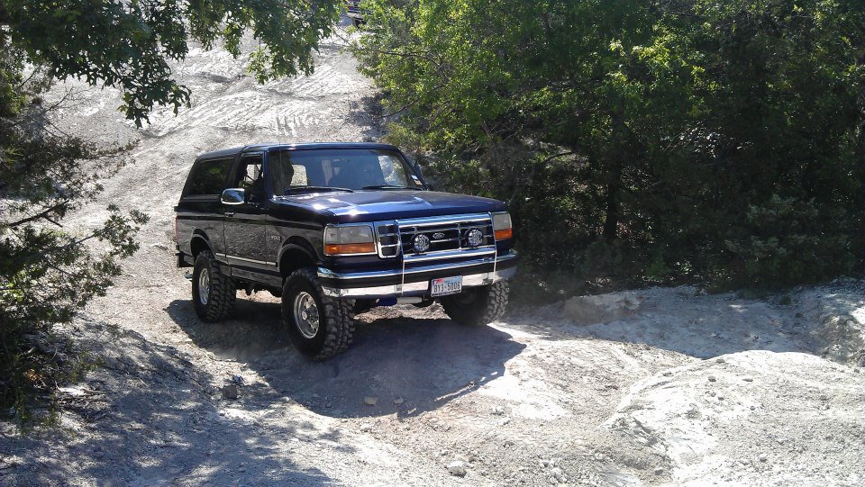 Dark blue Ford Bronco driving on a dirt trail with trees and rocks