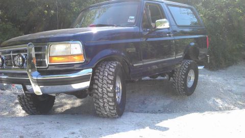 1995 Ford Bronco - This blue 1995 Ford Bronco is equipped with large off-road tires and appears to be navigating a dirt trail.