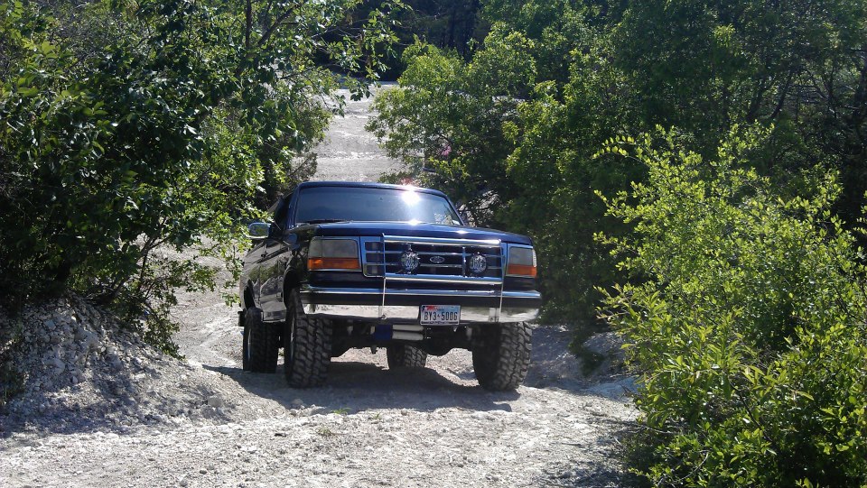 1995 Ford Bronco driving up a rocky, wooded trail