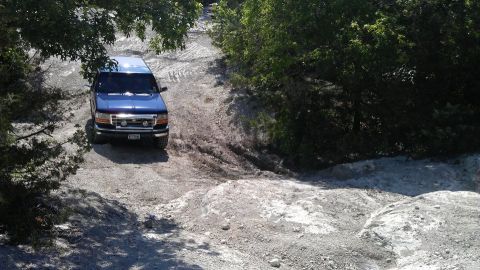 1995 Ford Bronco - A blue SUV navigates a challenging off-road trail under a sunny sky.