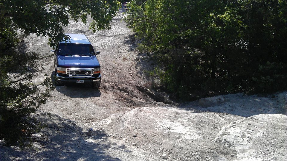 Blue SUV driving on a rough dirt road with trees around