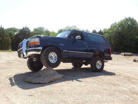 1995 Ford Bronco - A dark blue 1995 Ford Bronco navigates an obstacle on a dirt lot.