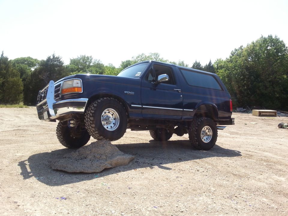 Dark blue 1995 Ford Bronco with lifted suspension and off-road tires, front driver's side tire on a rock