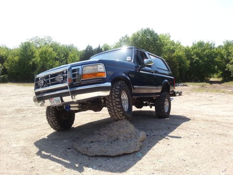 1995 Ford Bronco - This Ford Bronco is navigating an obstacle on a dirt road with trees in the background.