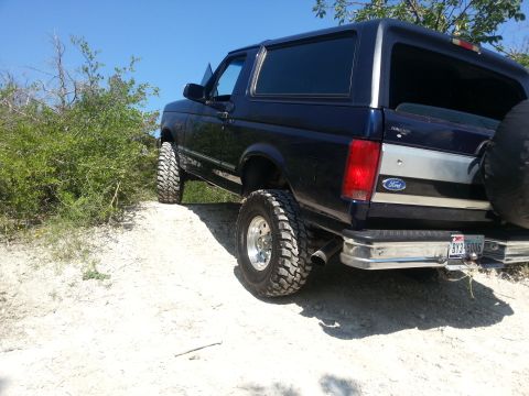 1995 Ford Bronco - Ford Bronco with aftermarket wheels and tires driving on a dirt trail.
