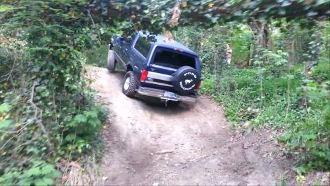 1995 Ford Bronco - A Ford Bronco navigates a steep, wooded trail during a hill climb event.
