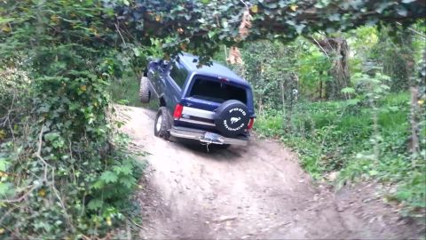 1995 Ford Bronco - Ford Bronco navigates a challenging off-road trail, kicking up dust on the steep incline.