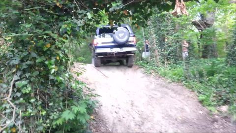 1995 Ford Bronco - A dark blue Ford Bronco navigates a steep, overgrown dirt path.