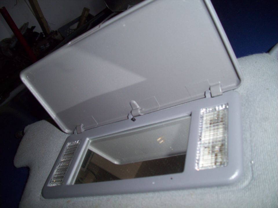 Gray sun visor with open lid, vanity mirror, and illuminated light covers