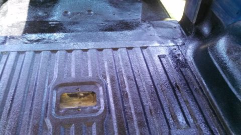 1979 Ford Bronco - The ribbed texture of a black truck bed liner is visible, with a metal access panel in the center.