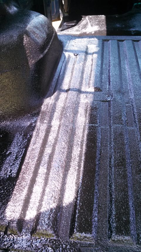 1979 Ford Bronco - Newly applied black spray-on liner covers the ribbed floor and wheel well of a truck bed.