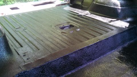 1979 Ford Bronco - The interior floor of a vehicle shows a textured black coating over ribbed metal panels.