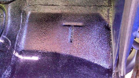 1979 Ford Bronco - The underside of a vehicle shows a textured black coating with a prominent T-shaped indentation, suggesting a specific part or structural e…