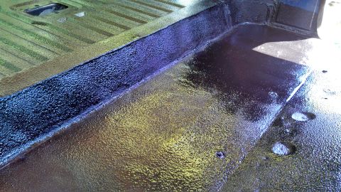 1979 Ford Bronco - The interior floor of a vehicle shows a textured protective coating with a raised seam and a square cutout visible.
