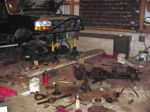 1992 Ford Bronco - A vehicle is disassembled in a garage, with various parts scattered around the floor.