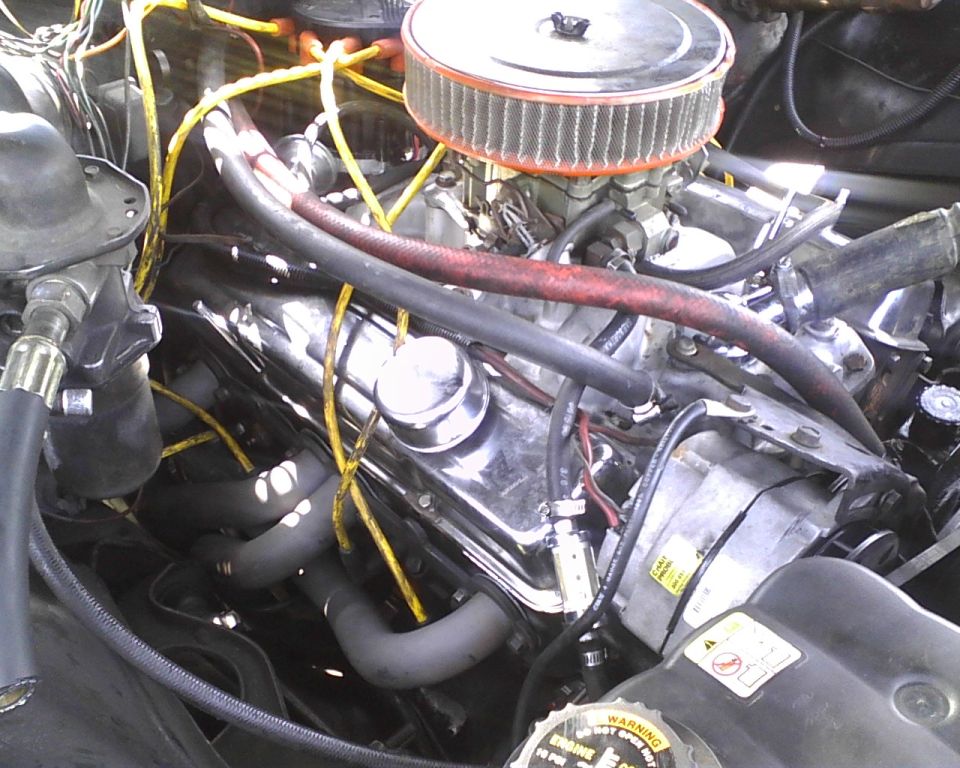Close-up of a V8 engine bay, showing chrome valve covers, air filter, hoses, and wiring. SuperMotors logo visible