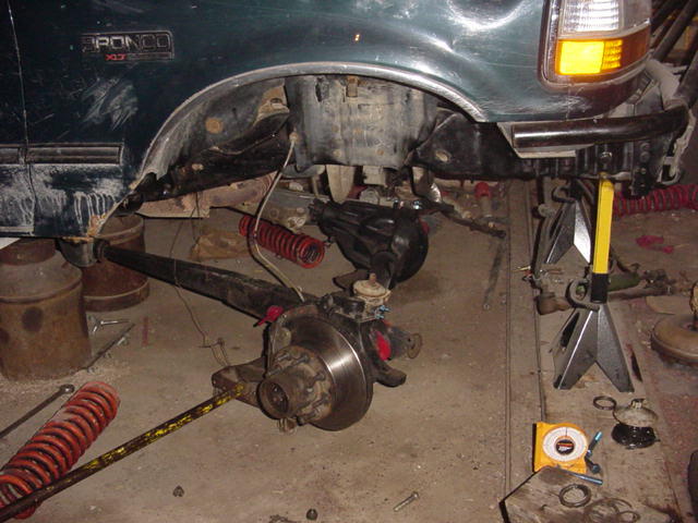 Green 1992 Ford Bronco front suspension disassembled, supported by jack stands