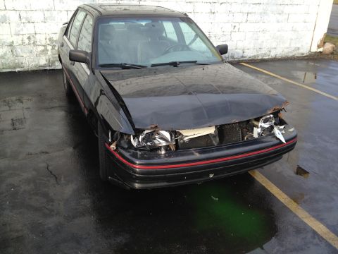 1988 Ford Bronco - A black sedan sits with significant damage to its front end, including a crumpled hood and broken headlights.