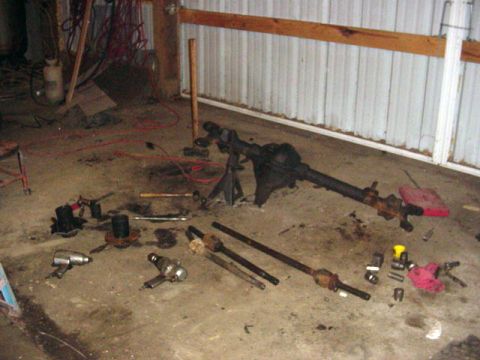 1992 Ford Bronco - A disassembled vehicle axle and various parts are laid out on the concrete floor of a workshop.