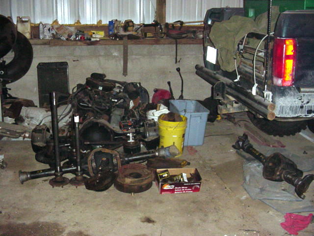Truck rear end and various disassembled vehicle parts like axles and engine components are on the floor of a garage