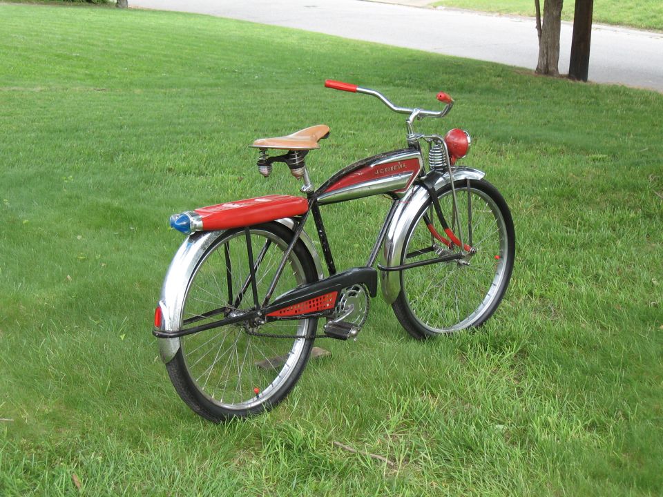 Red and chrome bicycle with a tan seat and red tail light, parked on grass