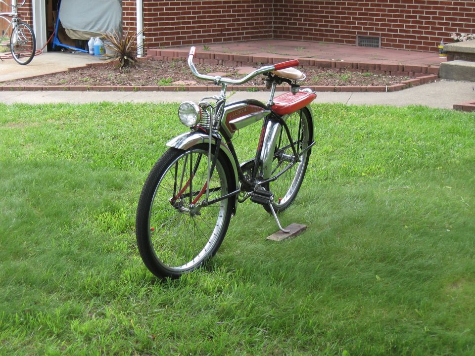 Vintage bicycle with red seat and handlebars parked on grass, another bicycle visible in garage background