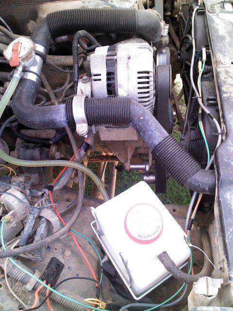 1987 Jeep Comanche - Close-up view of the engine bay, focusing on the alternator and various hoses and wiring.
