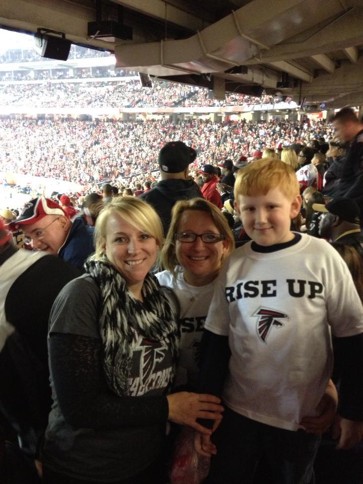 Three people in stadium seats, two women and a boy wearing Atlanta Falcons shirts