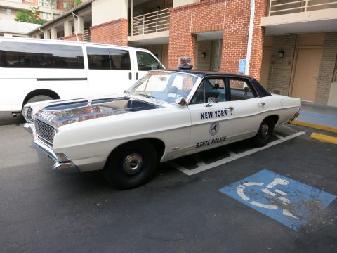1991 Ford LTD Crown Victoria - white-and-black classic Ford New York State Police sedan sits in a handicap space beside a white van and brick building.