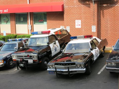 1991 Ford LTD Crown Victoria - black-and-white Dodge police pickup and a Dodge police sedan park nose-in among cruisers by a brick restaurant.
