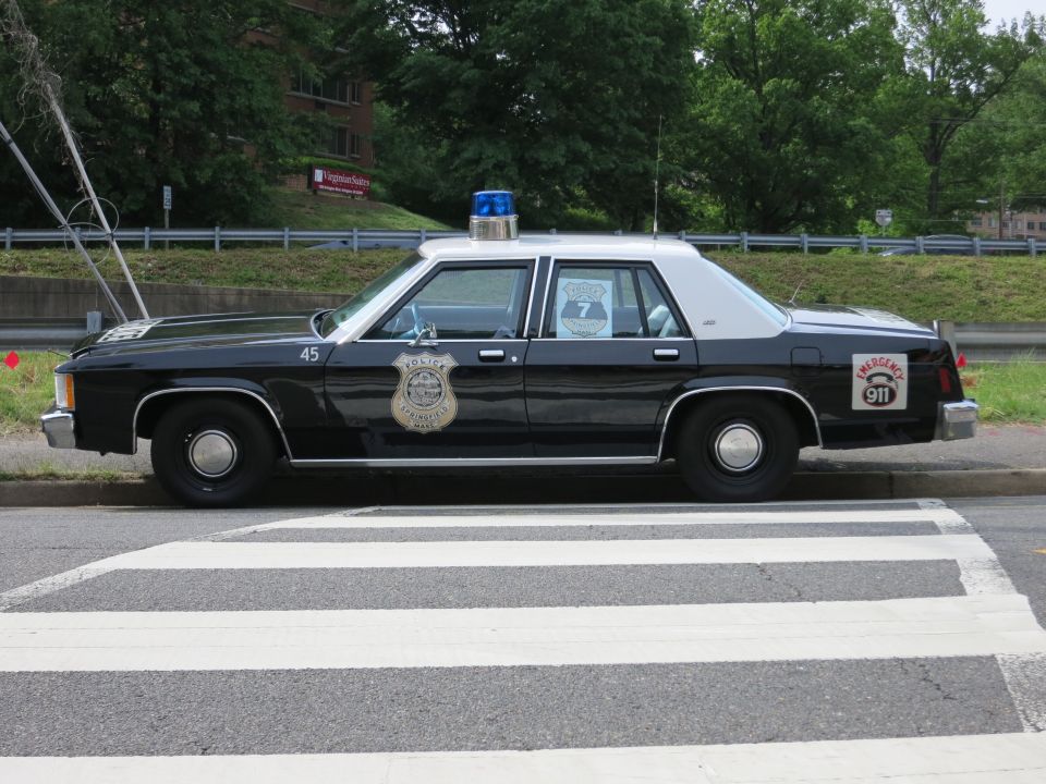 Black-and-white Ford LTD police sedan with badge emblem parked over a crosswalk