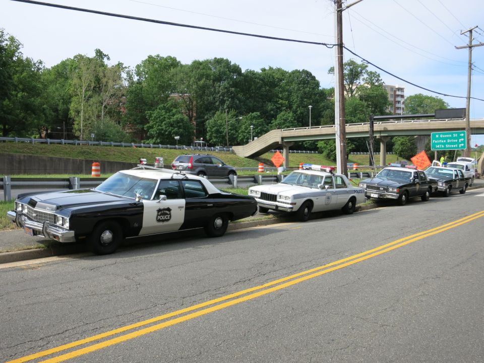 Row of vintage black-and-white and tan POLICE cruisers parked along a roadside