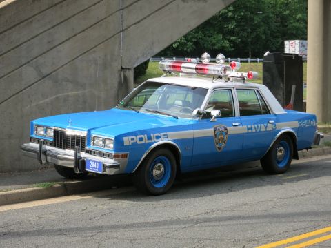 1991 Ford LTD Crown Victoria - two-tone blue NYPD-style highway sedan marked POLICE HWY with a full roof lightbar is parked under an overpass.