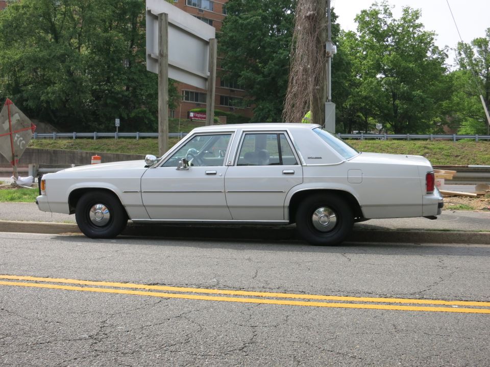 Plain white full-size sedan parked at the curb on a tree-lined street