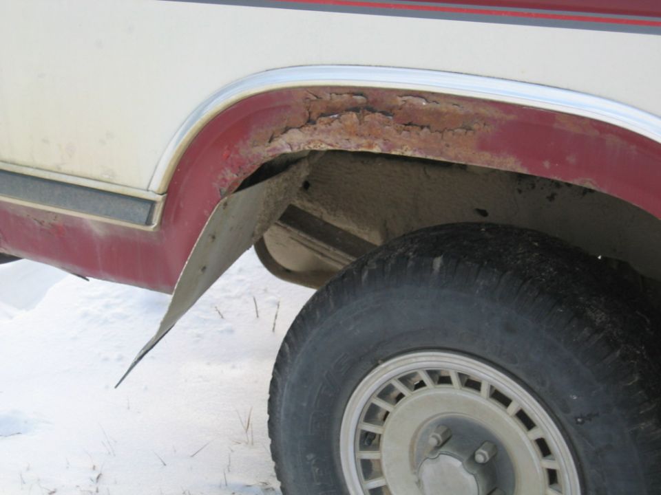 Rear wheel well of a vehicle with significant rust and a detached mud flap