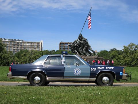 1991 Ford LTD Crown Victoria - two-tone blue 90E STATE POLICE sedan sits on grass in front of the Iwo Jima flag-raising statue under a partly cloudy sky.