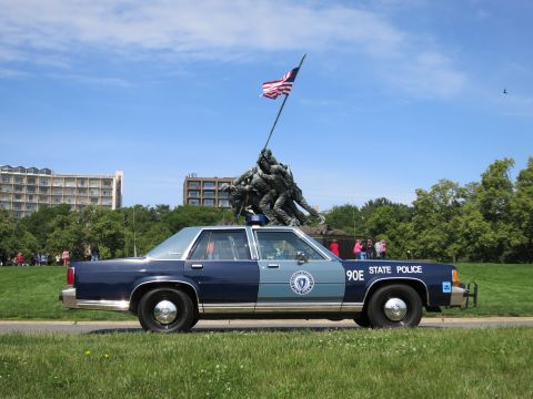 1991 Ford LTD Crown Victoria - two-tone blue 90E STATE POLICE sedan is parked on grass with the Iwo Jima memorial and onlookers in the background.