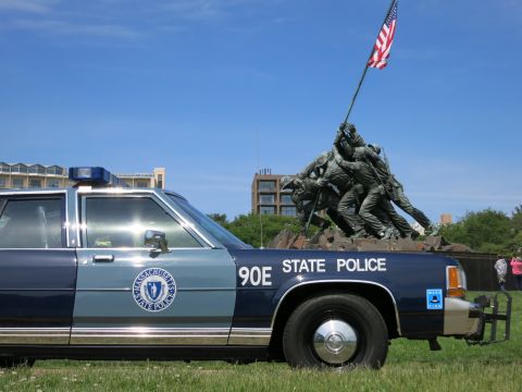 1991 Ford LTD Crown Victoria - close front-quarter view of a blue 90E STATE POLICE sedan with a roof beacon and department seal, the Iwo Jima statue rising behind.