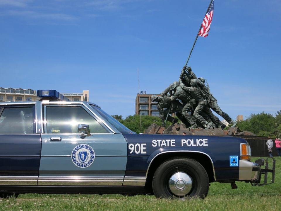 Close view of a blue 90E STATE POLICE sedan front quarter with the Iwo Jima Memorial behind