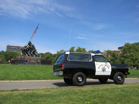 1991 Ford LTD Crown Victoria - black-and-white Highway Patrol SUV with rooftop light parked on a path near a bronze flag-raising war memorial.