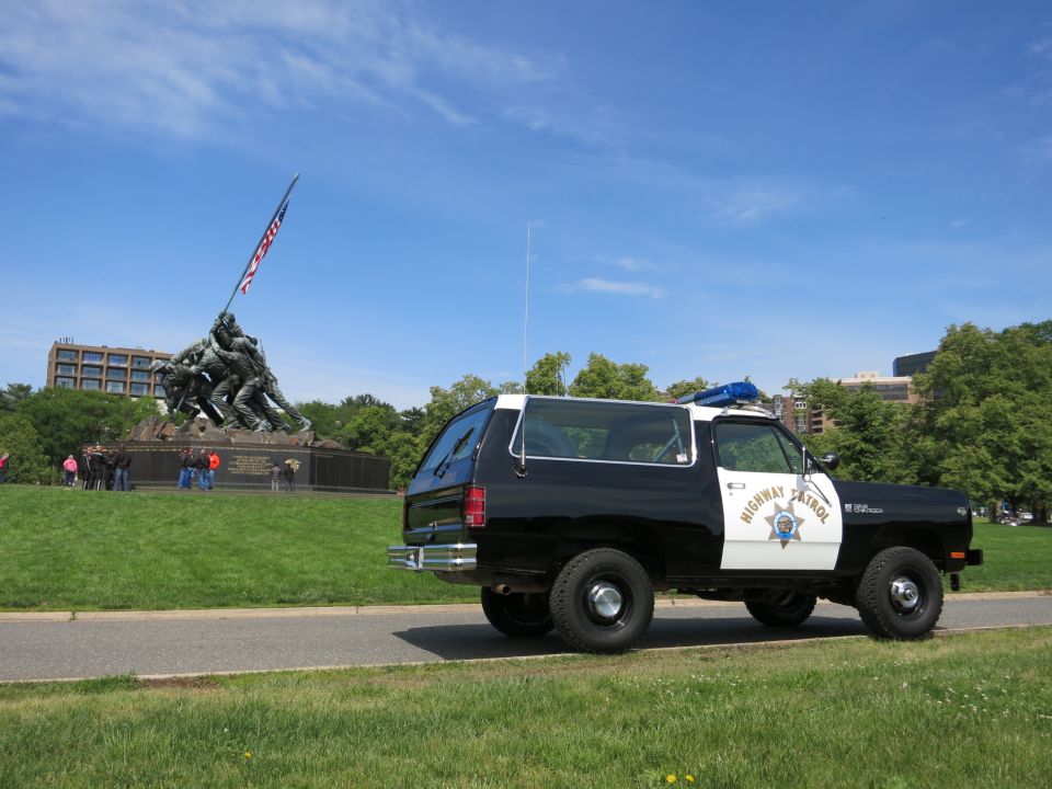 Black and white Highway Patrol SUV parked near a war memorial with a U.S. flag